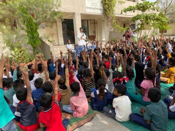 a group of children sitting on the ground with a person standing in front of them at Shree Danev Foundation.