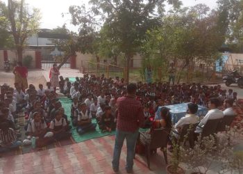 Children sitting on the ground in front of a gathering of adults, highlighting the Shree Danev Foundation's outreach efforts.