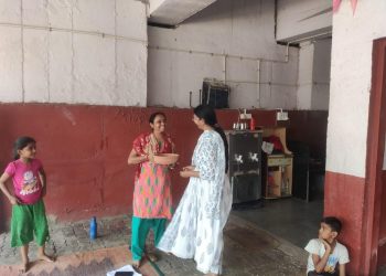 At the Shree Danev Foundation's pot distribution camp, a woman in a pink dress converses with two children.